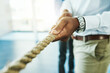 © Tamani Chithambo/peopleimages.com - Business, man and hands with rope for tug of war in office with team building, competition and fun game. Professional, employee and collaboration for challenge and conflict resolution in workplace