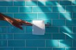 © Nyxoria - Hand reaching for a roll of white toilet paper on a chrome holder against a turquoise tiled wall in bright sunlight