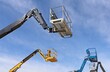 © luca piccini basile - Four aerial working platforms of cherry pickers against blue cloudy sky.