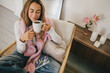 © polinaloves - Young woman with long hair drinking tea, sitting on a chair in a cozy living room.