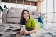 © deagreez - Smiling young woman lying on living room carpet enjoying a relaxing afternoon indoors while using smartphone in bright modern home