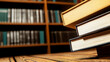 © nuttachet chinavong - Books stacked on wooden table in library, showcasing their colorful spines against blurred background of shelves filled with more books
