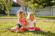 © Lena May - Two cute girls in party hats sitting on grass and blowing soap bubbles outdoors in sunny backyard