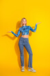 © deagreez - Stylish young woman in modern casual outfit spreading arms against vibrant yellow vertical background in a confident pose