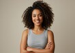 © Laki - Portrait of a smiling woman with curly hair and arms crossed wearing a gray tank top on beige background