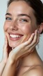 © natakot - A stunning young woman with flawless, glowing skin beams with joy, her hands gently framing her face. Her bright smile and sparkling eyes radiate happiness and confidence, inviting viewers to share in