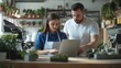© Moh - Two individuals collaborate on a laptop in a cafe.  They're focused on a digital task, likely business-related, in a bright, plant-filled environment