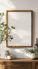 Fototapete - A wooden frame sits empty against a softly lit wall, surrounded by lush greenery and elegant glass vases on a wooden surface, creating a serene and inviting atmosphere