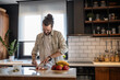 © Migma_Agency - Smiling man cutting radishes and preparing a fruit salad in a modern kitchen