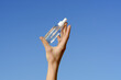 © Daryna  - Female hand holding a transparent glass jar of serum with a pipette dispenser on a blue sky background. Concept of beauty and aesthetics products, cosmetics for moisturizing the skin