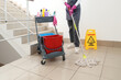 © Pixel-Shot - Female janitor with trolley of cleaning supplies mopping floor in stairway
