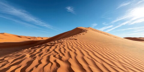 Aufkleber - Sandy desert landscape under a bright blue sky with wispy clouds. The foreground features large sand dunes with distinct ripple patterns bathed in warm sunlight