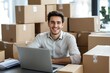 © ffunn - Handsome young man, smiling businessman is sitting at his desk in the office, surrounded by working on an online store, ready to ship goods for customers throughout the country