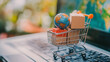 © Bnz - Miniature shopping cart filled with cardboard box and a small globe on a laptop keyboard with blurred map background. Concept of global e commerce, logistics, online retail and international shipping.