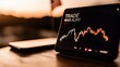 © dinatychynska - A digital tablet displays TRADE WAR ALERT with a volatile stock chart, symbolizing financial instability and economic uncertainty. A blurred American flag is visible in the background.