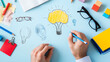 © Somporn Na Ubon - Creative brainstorming session with hands drawing ideas on blue background, featuring light bulbs, skull, and various stationery items
