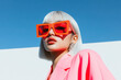 © Papukos - Fashion model wearing orange sunglasses and pink jacket posing under blue sky