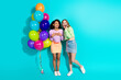 © deagreez - Two joyful young women with colorful balloons, standing against a vibrant teal background
