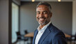 © f_bossa - Modern portrait headshot of a friendly ceo executive business worker: A smiling, mature man with graying hair and a neatly trimmed beard confidently poses in a navy suit and open-collared white shir