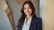 © f_bossa - Modern portrait headshot of a friendly ceo executive business worker: A confident businesswoman with long dark hair smiles directly at the camera while leaning against a modern architectural wall.