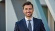© f_bossa - Modern portrait headshot of a friendly ceo executive business worker: A smiling, well-dressed man in a suit confidently poses outdoors in front of a modern architectural building.