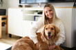 © Louis-Paul Photo - Portrait of a young woman on the livingroom with golden retriever dog indoors at home.