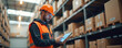 © Pete - Warehouse worker manages smart logistics, using tablet for order, shipment tracking. Man in orange helmet vest works with digital interface, modern tech, automation in delivery. Boxes, pallets, goods