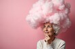 © Pete - Elderly woman with cloud shaped head, pink background. Concept mental health, memory loss, dementia, brain fog. Thoughtful senior female looks up, contemplates thoughts. Mind, thinking, creativity,