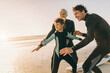 © Marko Geber - Multigenerational family of male surfers getting ready to surf on a sandy beach
