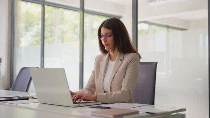 Young professional it specialist latin hispanic business lady working on laptop pc sitting at desk in modern office space. 30s middle eastern indian woman using computer technology app for work online