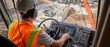 © hobday - A crane operator in a high-visibility vest and helmet, operating the crane controls with a view of the construction site through the cab闁炽儲鐛�window, Construction site scene