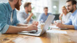 © Tossakan Photos - Team of professionals collaborating at a table with a laptop during a meeting in a bright, modern office setting.