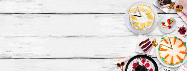 Leinwandbilder - Dessert side border with an assortment of cakes. Overhead view over a white wood banner background. Copy space. Black forest, lemon, carrot, red velvet, chocolate and cheesecakes.