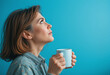 © JELENA - A woman is holding a white coffee cup and looking up. Concept of contemplation and relaxation, as the woman takes a moment to enjoy her coffee and gaze into the distance