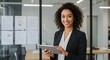 © Matheus - A woman with curly hair smiles while using a tablet in a modern office.