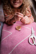 © Cavan - Child threading a needle while crafting on a pink textile surface