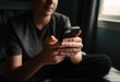 © Cavan Images - Close up of hands of teen boy holding smartphone sitting on bed.