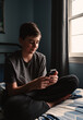 © Cavan Images - Close up of teen boy in bedroom using smartphone on his bed.