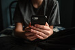 © Cavan Images - Close up of hands of teen boy holding smartphone sitting on bed.