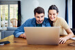 © baranq - Young couple at home using laptop together sitting at dinning table in living room