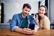 © baranq - Couple with whippet dog at home having fun at a table talking selfie