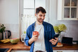 © baranq - Portrait of young man in kitchen using mobile phone while having coffee