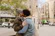 © Drobot Dean - A cute gay couple of a Black man and a White man, who are in their 30s, standing on a city street and kissing lovingly, on a sunny day, with cars and shops in the background