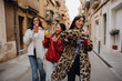 © Drobot Dean - Three diverse women walk down a city street enjoying drinks and each other's company. One wears a white coat, another a red jacket, and the third a leopard-print coat during their conversation.