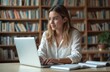 © miss irine - Young woman student using laptop, studying, researching in library. Female student learning, browsing online resources at college, university. Student desk with opened book. Education, e-learning
