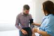 © AntonioDiaz - Nurse taking blood pressure of a male patient during medical consultation in a modern doctor's office