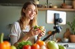 © miss irine - Young woman vlogging about healthy food, cooking in kitchen. Holds salad in glass bowl, smiling, records video on smartphone. Healthy eating concept, social media influence, home online communication.