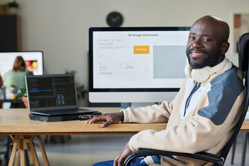 Fototapete - Young successful African American male programmer looking at camera while sitting by workplace with two computers