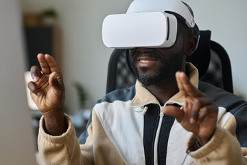 Fototapete - Young smiling African American man scrolling through virtual presentation or information in VR headset while sitting in office