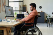 © pressmaster - Side view of young multiethnic man with disability sitting in wheelchair and typing on keyboard while using AI image generator